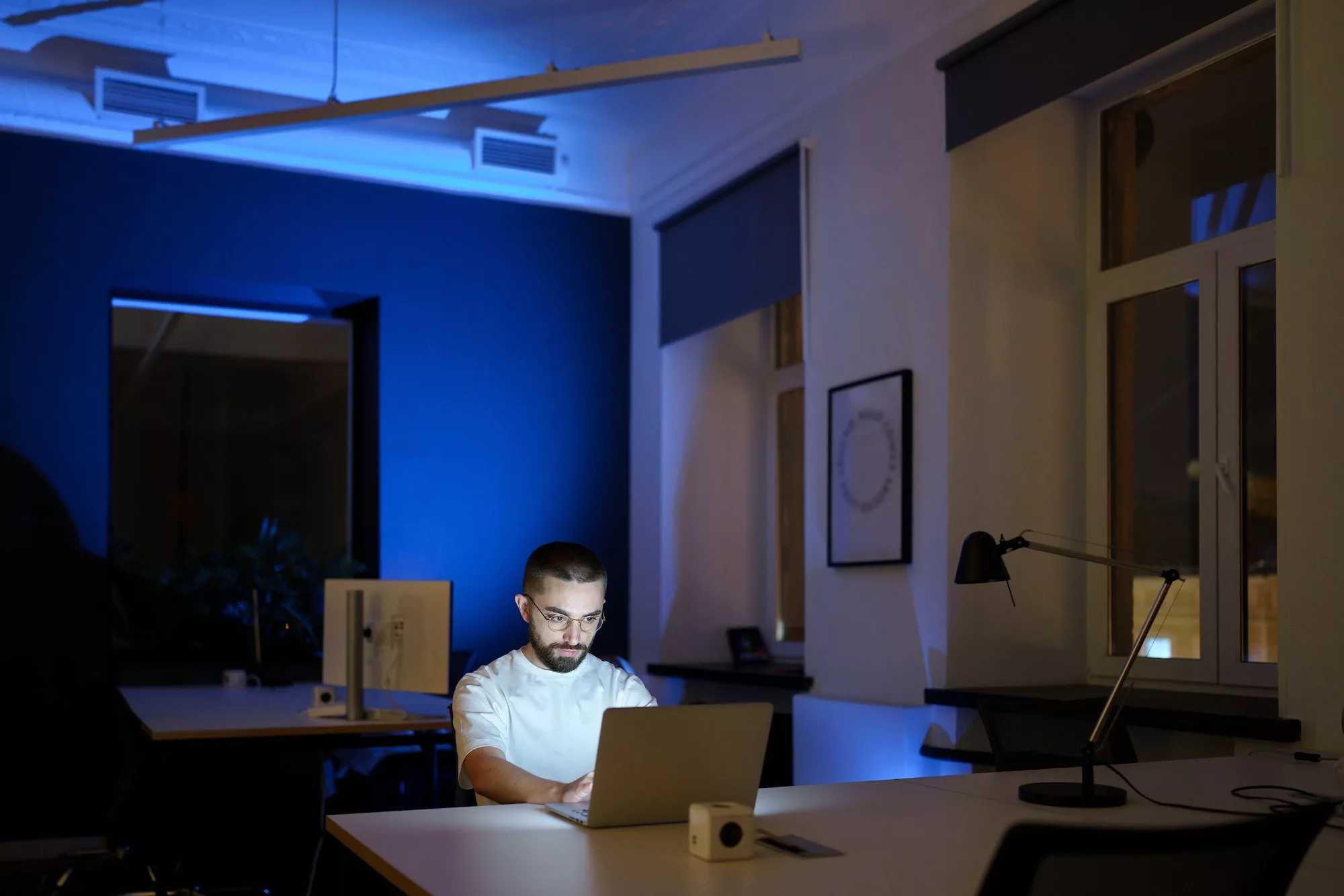 Concentrated man web designer in eyeglasses stay in office overtime work on project at dark night
